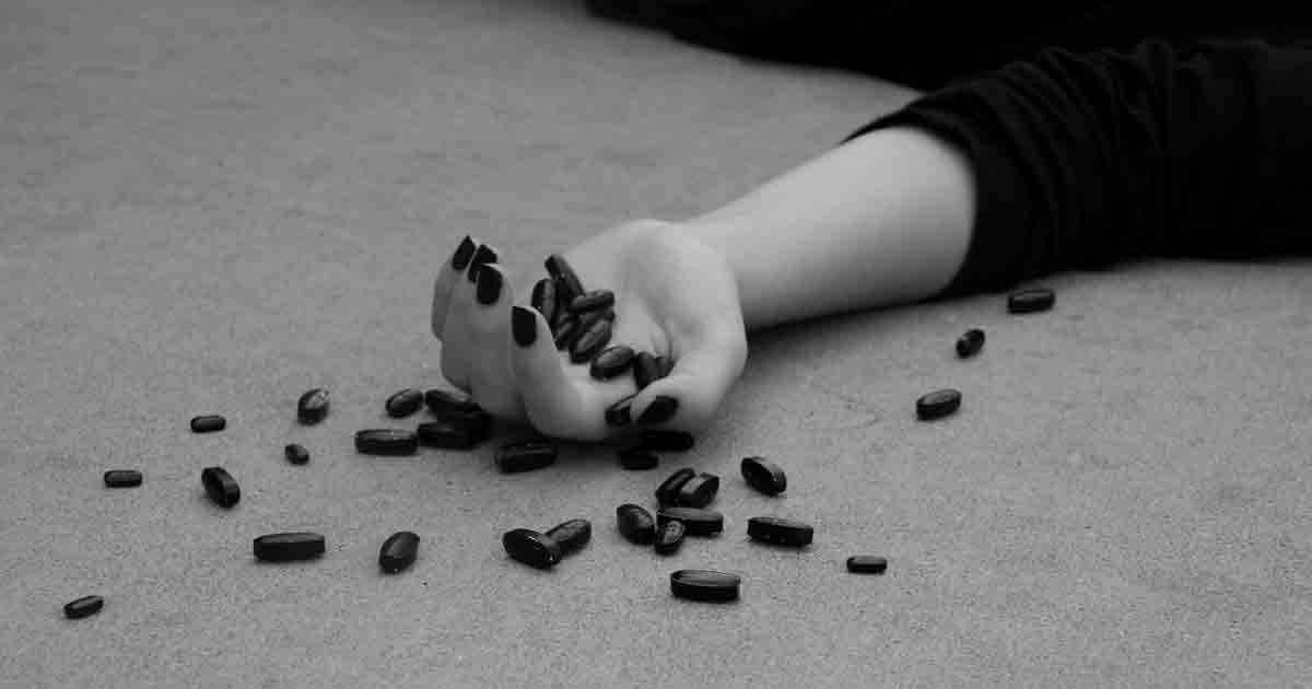 L'immagine, in bianco e nero, mostra la mano di una ragazza evidentemente svenuta contenente alcune pillole scure