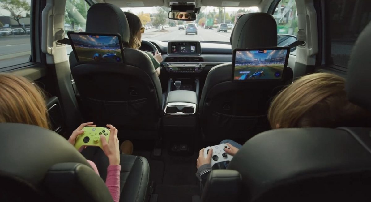 Dei bambini videogiocano con dei joypad Xbox, mentre sono seduti sui sedili posteriori di un'auto, direttamente sugli schermi del veicolo.