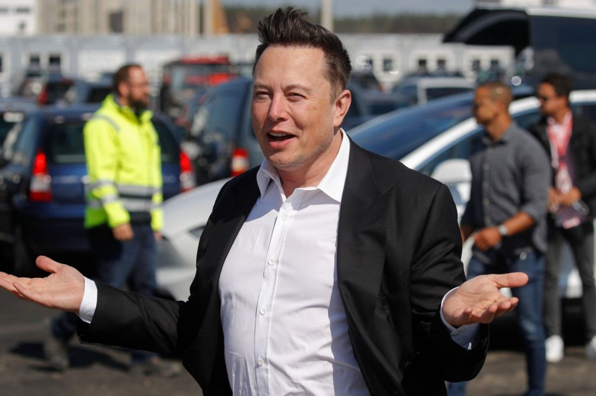 Elon Musk alza le braccia sorpreso e sorridente.