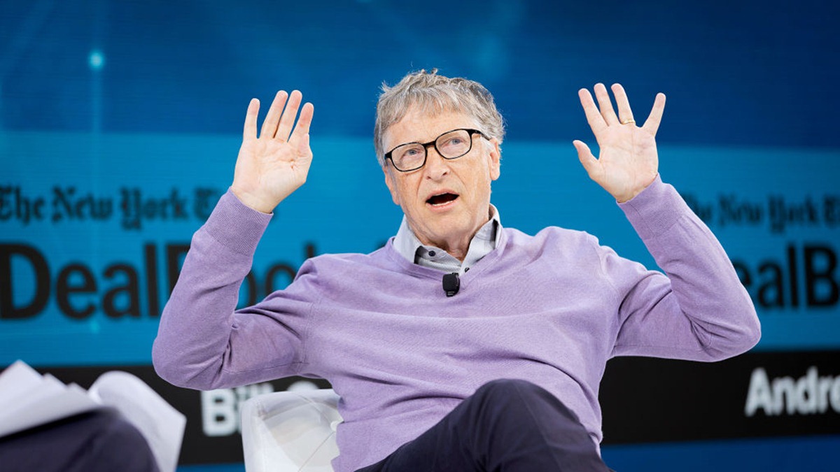 Bill Gates alza le mani mentre gesticola durante una confferenza.