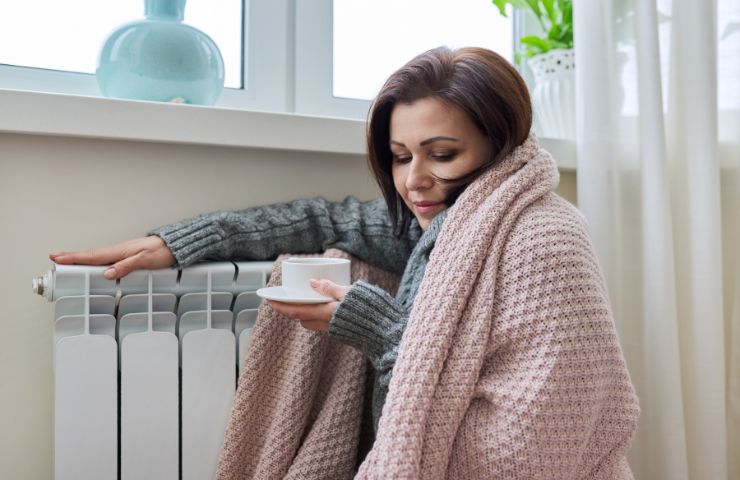 donna accanto al termosifone con coperta e bevanda