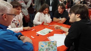 Un gruppo di persone siede attorno al tavolo con mappe e schede giocando a last resort