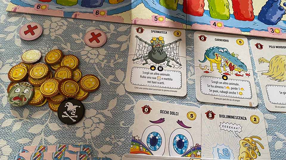 Dettaglio del tavolo di gioco di Evolversi Male con gettoni evoluzione e carte nel mercato