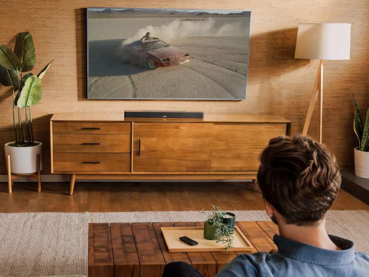 un ragazzo al divano con davanti un tavolino e una tv con soundbar