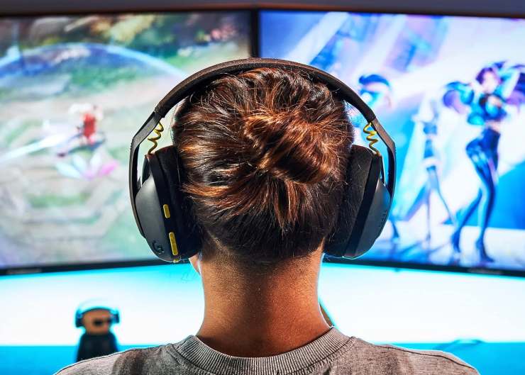Un ragazzo con delle cuffie da gaming di fronte a due monitor