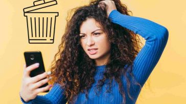 donna riccia vestita di blu che si mette le mani nei capelli e guarda lo smartphone