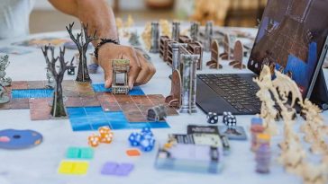 persona che sta posizionando il modellino di un pozzo sul gioco da tavolo