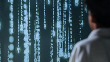 Un uomo di fronte a un enorme sfondo con codici binari di un programma