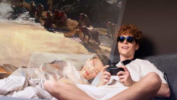 ragazzo con gli smart glass che gioca ai videogiochi steso sul letto mentre una ragazza dorme di fianco a lui