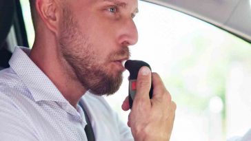 uomo con una camicia bianca che soffia nell'alcolock per far partire la macchina