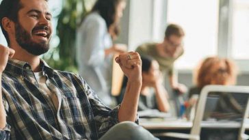 uomo in ufficio che alza i pugni contento