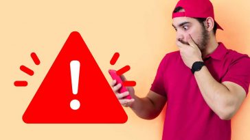 uomo preoccupato vestito di rosso che guarda lo smartphone con il simbolo di pericolo accanto