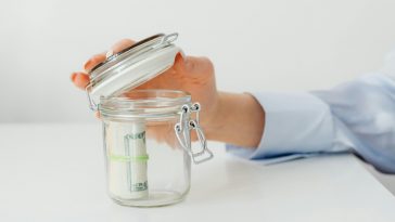 Un barattolo con dei risparmi e una mano che lo apre
