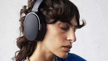 ragazza con capelli ricci e collana perle ascolta musica con cuffie a occhi chiusi ed espressione concentrata