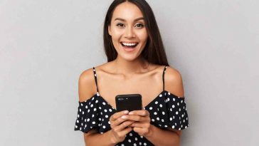 donna con vestito a pallini che sorride con lo smartphone in mano