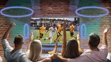 Persone esultano guardando televisione appesa al muro