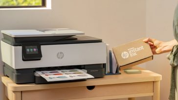 Stampante HP su tavolinetto di legno con accanto scatolo di cartucce Instant Ink
