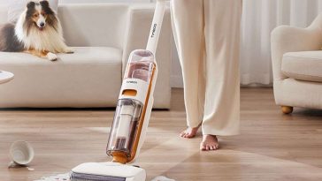 persona che usa la lavapavimenti Tineco IFloor Y2 per pulire macchie di latte sul pavimento di casa mentre c'è un cane dietro sul divano