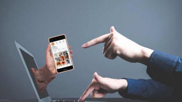 mano che indica smartphone che esce dallo schermo di un pc