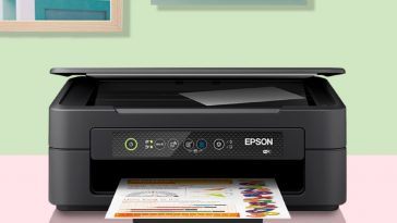 stampante epson appoggiata sul tavolo mentre stampa un foglio con alle spalle parete con quadri