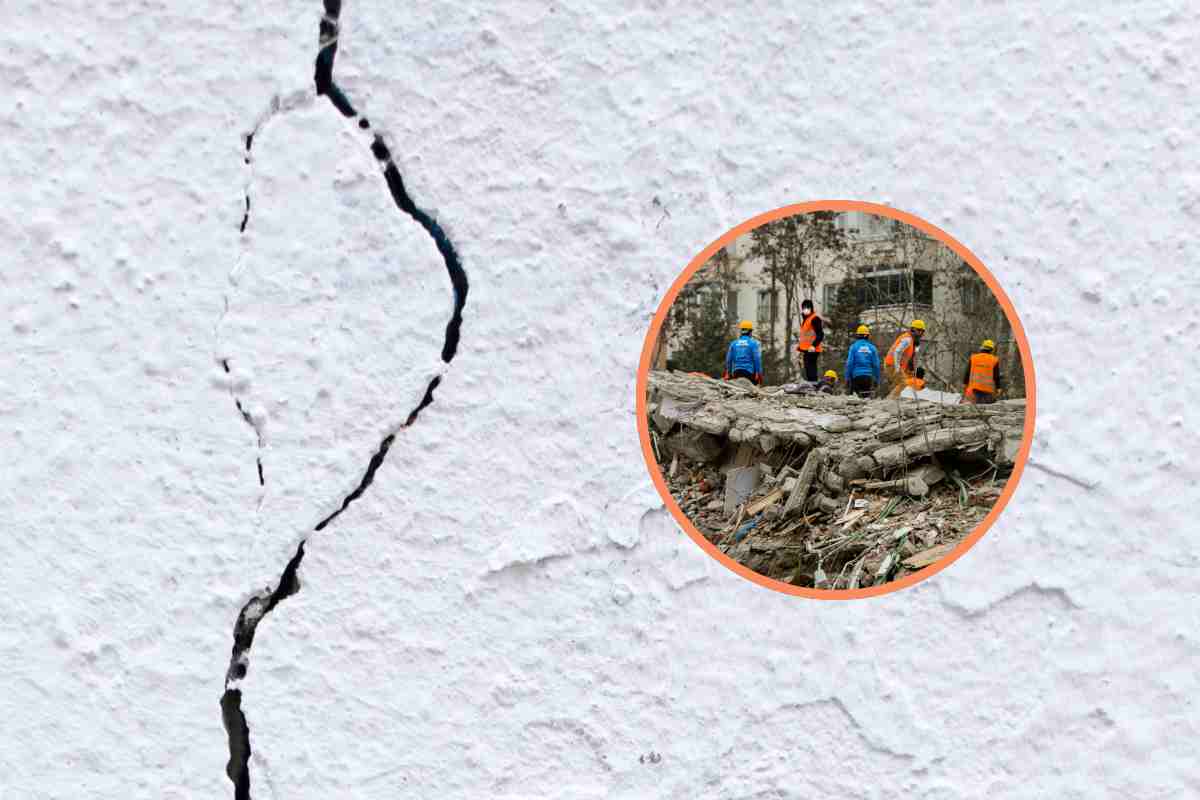 Una crepa in un muro e, in evidenza, degli operai davanti a un palazzo crollato