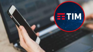 Una mano che regge un telefono vicino a un portatile e, in evidenza, il logo di TIM