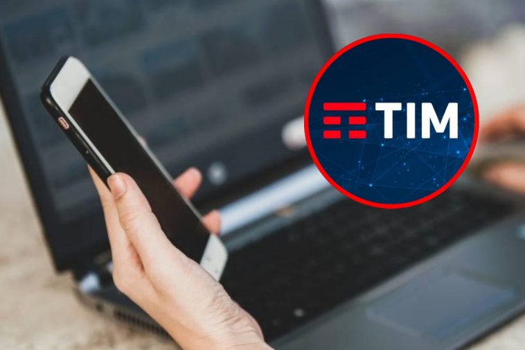 Una mano che regge un telefono vicino a un portatile e, in evidenza, il logo di TIM