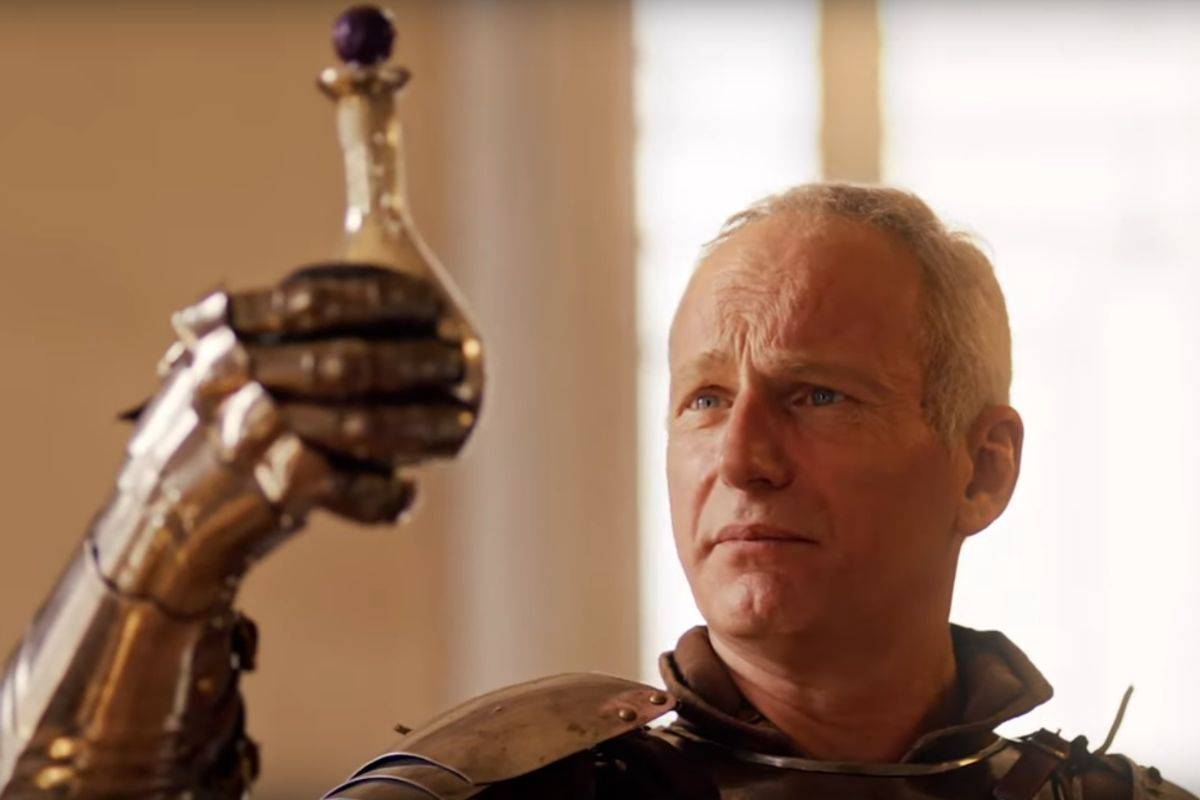 uomo con capelli grigi, armatura medievale e ampolla in mano