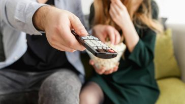 Due giovani guardano la tv con telecomando puntato e popcorn