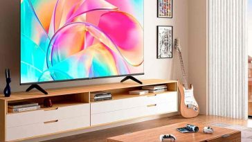 smart tv hisense appesa a parete in salotto con tavolinetto, parete attrezzata e chitarra elettrica