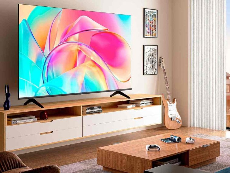 smart tv hisense appesa a parete in salotto con tavolinetto, parete attrezzata e chitarra elettrica