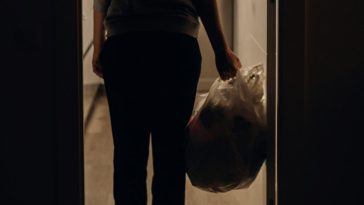 Una persona che si accinge a buttare un sacco della spazzatura