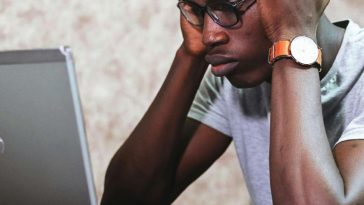 Un ragazzo con gli occhiali con le mani in testa di fronte a un portatile