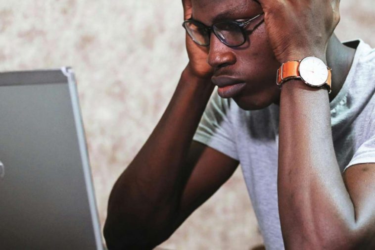 Un ragazzo con gli occhiali con le mani in testa di fronte a un portatile