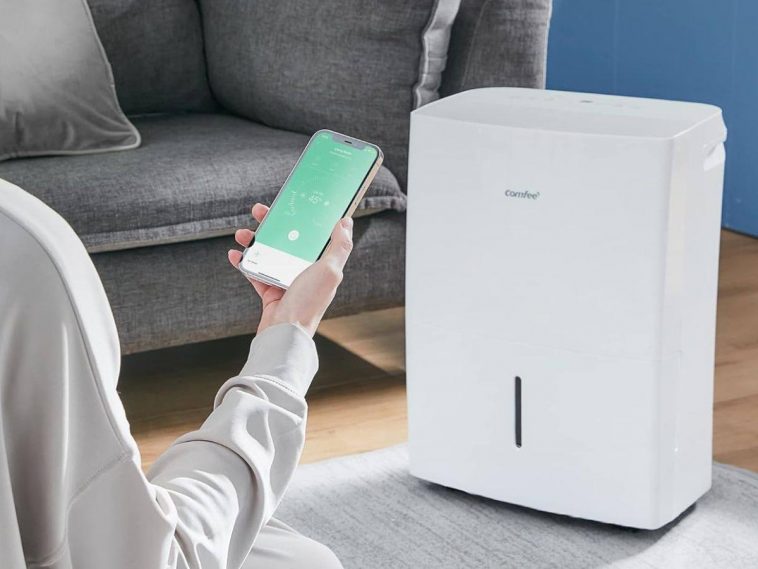 persona tiene in mano cellulare con app davanti a deumidificatore con divano