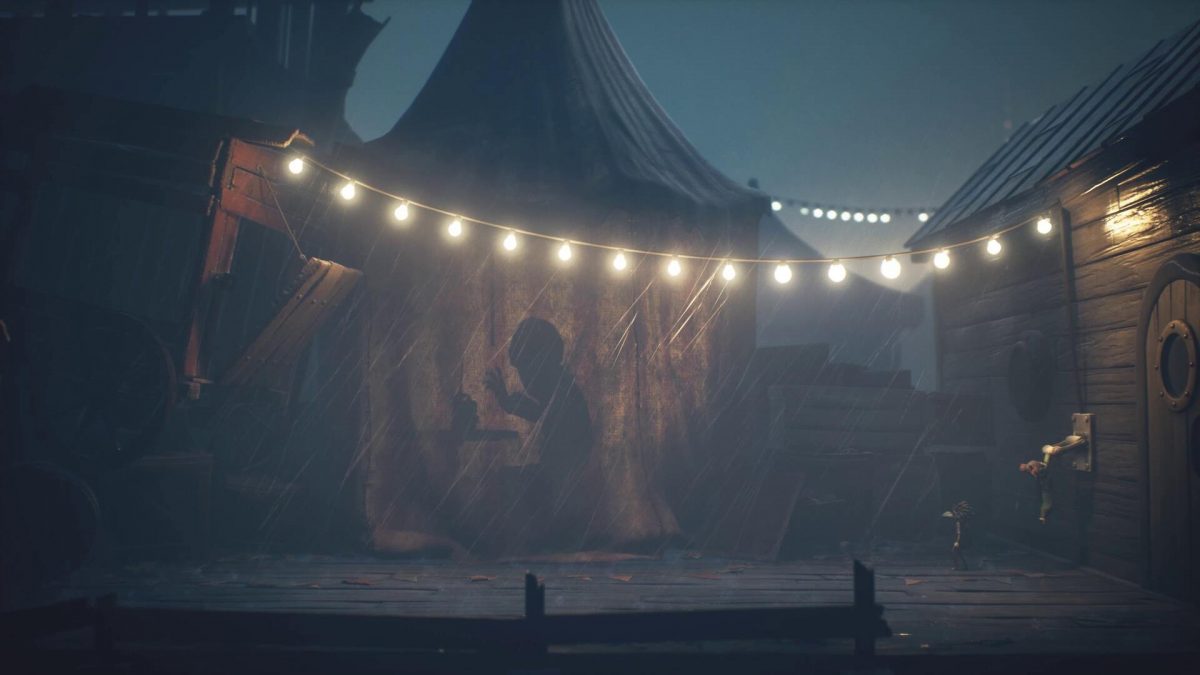 Una figura oscura si cela dietro una tenda di un circo mentre i protagonisti di Little Nightmares 3 tirano una leva