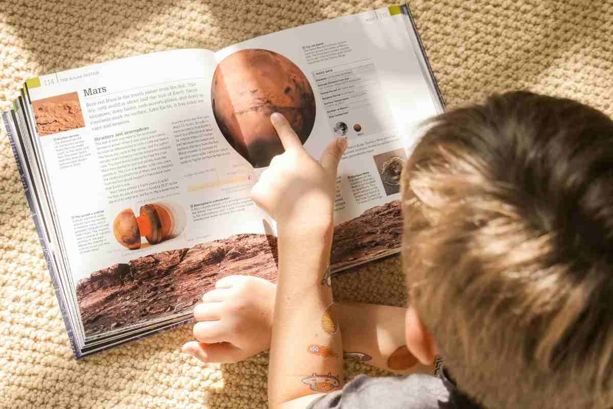 Un bambino che sfoglia un libro di astronomia e legge di Marte