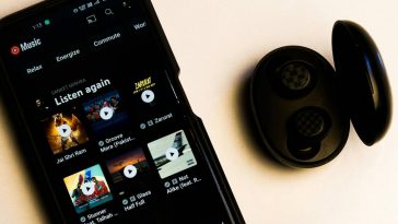 Uno smartphone con l'app YouTube Music in esecuzione e, accanto, delle cuffiette