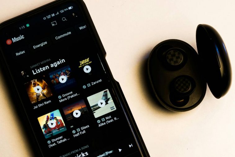 Uno smartphone con l'app YouTube Music in esecuzione e, accanto, delle cuffiette