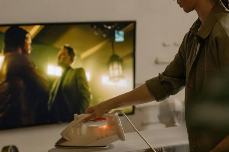 Una ragazza stira davanti alla tv accesa