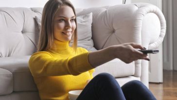 Una ragazza con un maglione giallo usa il telecomando