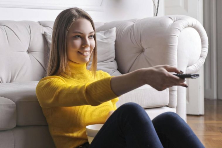 Una ragazza con un maglione giallo usa il telecomando