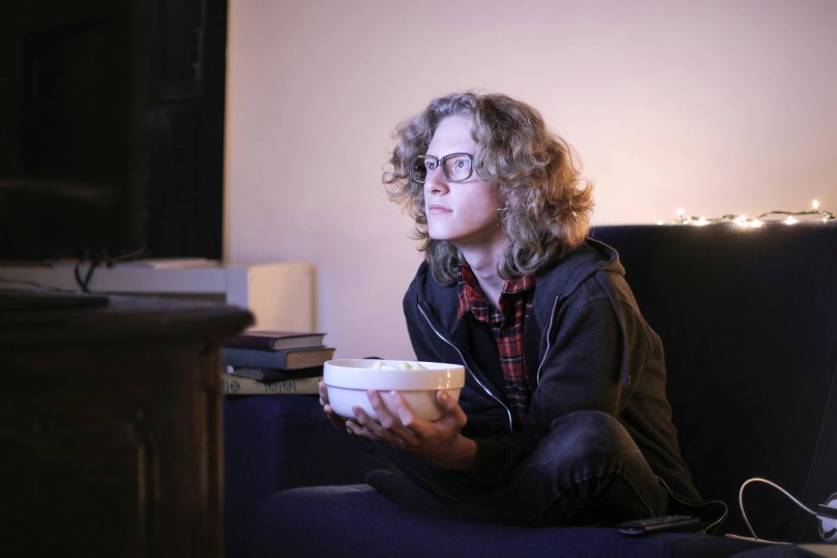 Un ragazzo con gli occhiali e una ciotola di pop-corn davanti alla tv