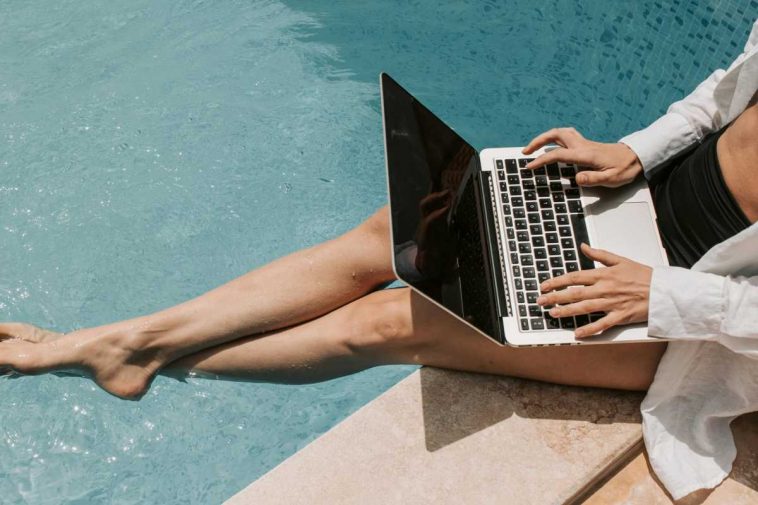 Ragazza a bordopiscina con un portatile sulle gambe