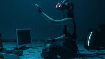 Una ragazza con un visore VR circondata da tastiere e computer