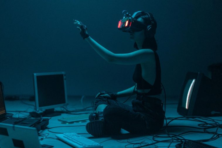 Una ragazza con un visore VR circondata da tastiere e computer