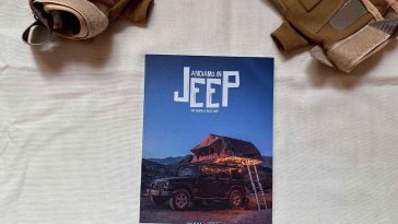 Un manualetto con la scritta andiamo in jeep e in copertina una jeep caricata per un campeggio e due guanti presenti sullo sfondo