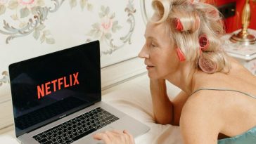 Una donna stesa al letto con i bigodini guarda Netflix da un laptop