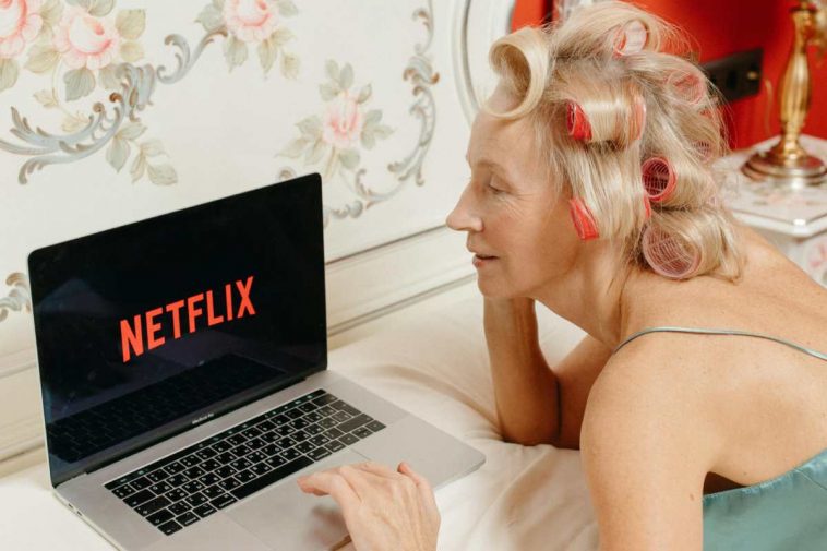 Una donna stesa al letto con i bigodini guarda Netflix da un laptop