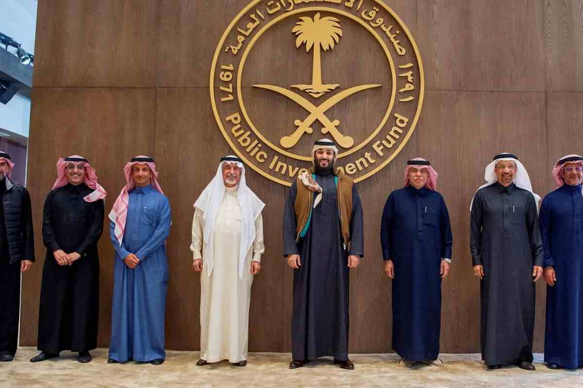 principe mohammad bin salman accanto a uomini in tunica e turbante, dietro logo Public Investment Fund